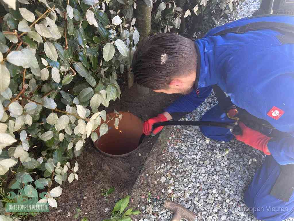 Een monteur voert een slang in een geopende rioolput in de tuin om het hoofdriool te ontstoppen in Vleuten